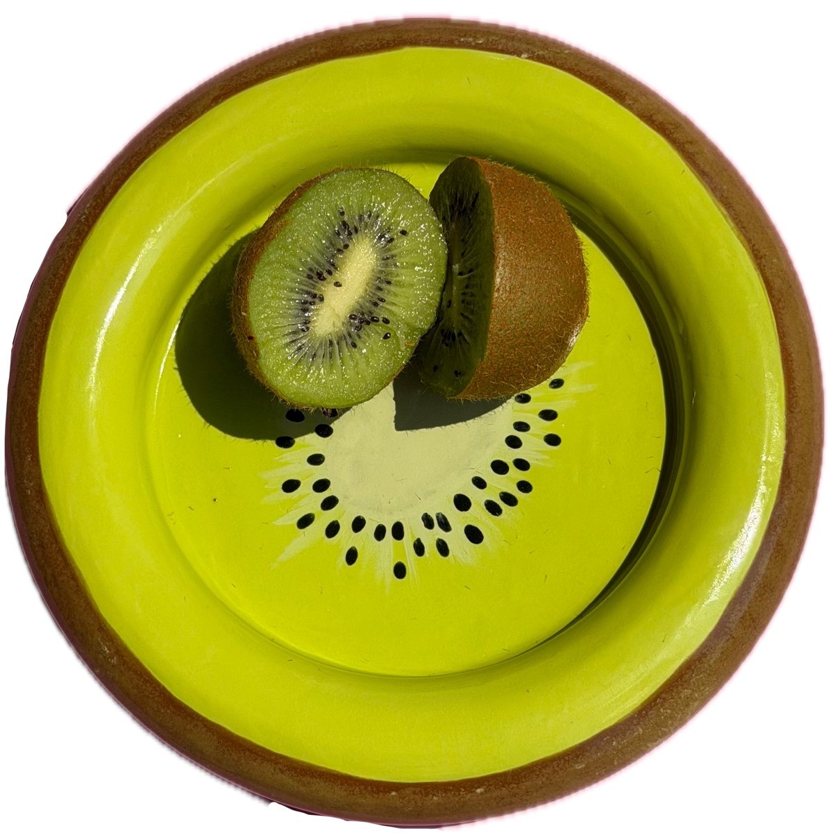 A round kiwi shaped ceramic plate with a bright lime green interior and a brown rim, shown from above with two halves of a sliced kiwi fruit placed inside the plate on a white background.