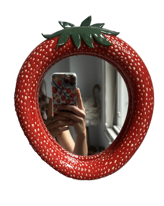 Strawberry-shaped mirror with a green stem on a white background. handmade ceramic mirror made in new york city